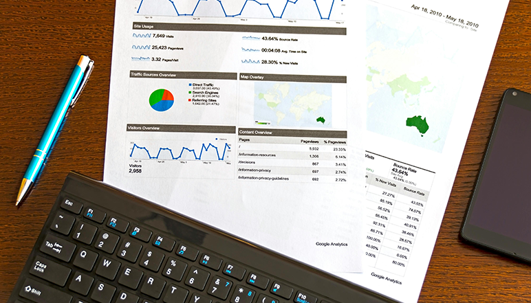 A keyboard and a pen next to printouts of Google Analytics reports with various charts and data.